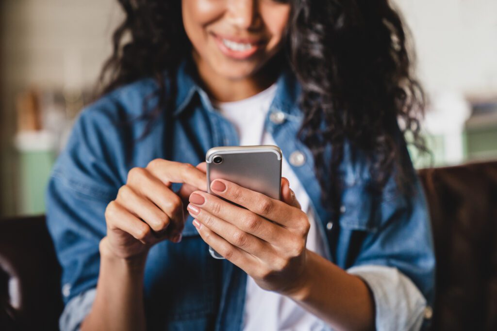 Cropped shot of an african-american young woman using smart phone at home.Smiling african american woman using smartphone at home, messaging or browsing social networks while relaxing on couch