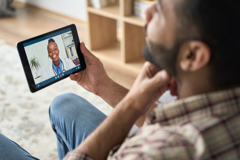Young indian latin bearded businessman having videocall meeting at home with black female healthcare doctor therapist using tablet computer pointing to throat. Online virtual telemedicine health care concept.