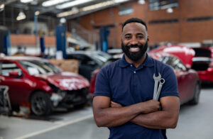 Portrait of a happy African American mechanic working at an auto repair shop and holding tools while looking at the camera smiling