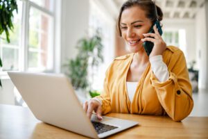 Happy business woman talking on a mobile phone and looking at a laptop screen.