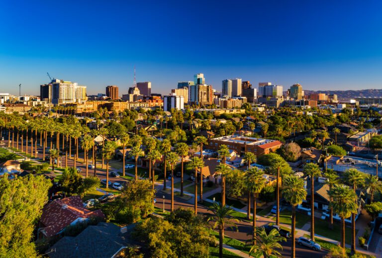 Aerial of Downtown Phoenix skyline with a residential neighborhood with many palm trees in the foreground.