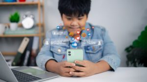Young boy using smartphone with social media reaction icons, chatting and online communication concept. Digital lifestyle, internet technology, children using mobile phone.