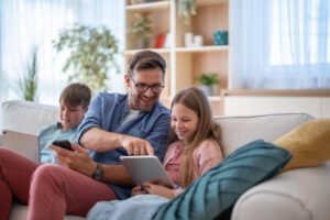Happy family using electronic devices while sitting on sofa in living room