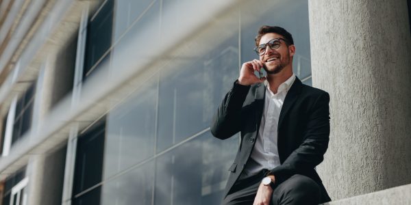 Smiling business person taking on mobile phone sitting outdoors Business man talking on a mobile phone.