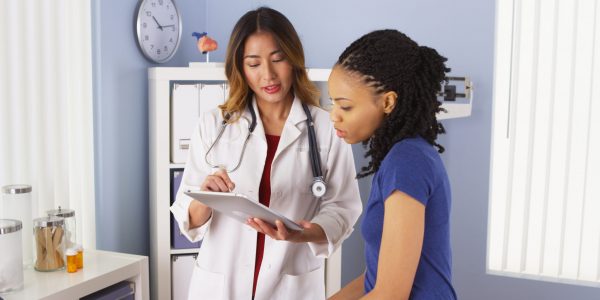African American patient explaining issues to Asian doctor using tablet HIPAA complaint business phone system for healthcare.
